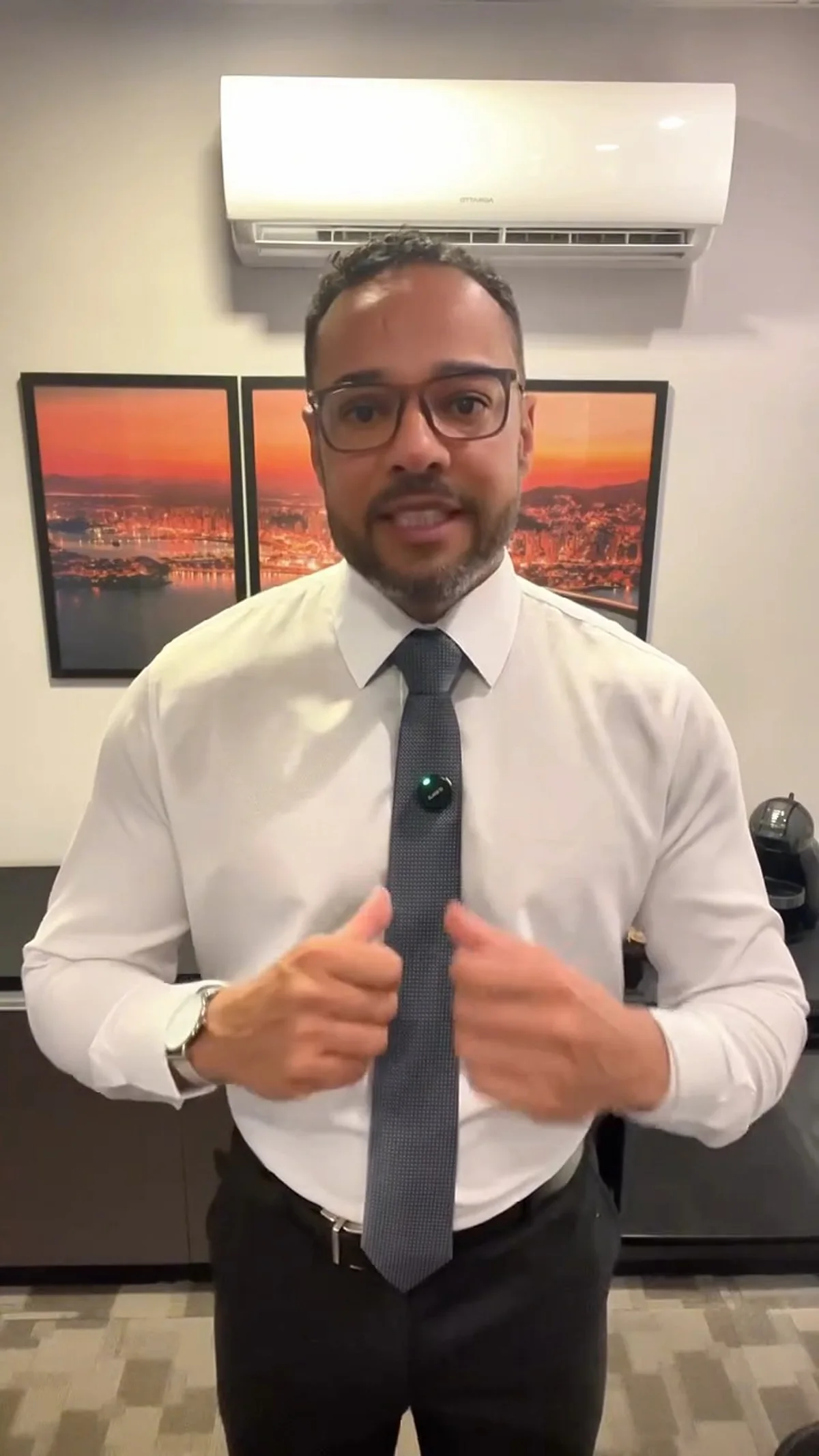 Wenddell Araújo, de camisa branca e gravata cinza, falando à câmera na sala do escritório, com as mãos à frente do corpo