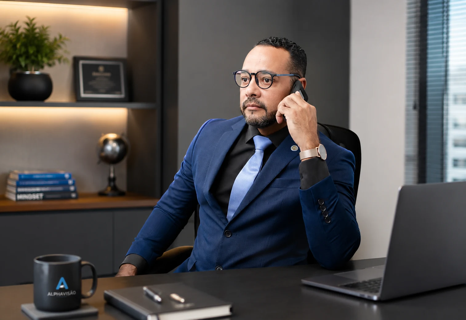 Wenddell Araújo, de terno azul e gravata azul-clara, ao telefone, sentado à mesa do escritório